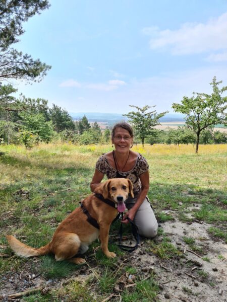 Frau sitzt mit Hund auf einer Wiese